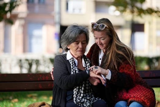 Elderly old cute woman with Alzheimer's very happy and smiling when eldest daughter hugs and takes care of her in park in autumn. Theme aging and parenting, family relationships and social care.