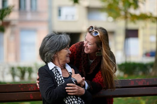 Elderly old cute woman with Alzheimer's very happy and smiling when eldest daughter hugs and takes care of her in park in autumn. Theme aging and parenting, family relationships and social care.