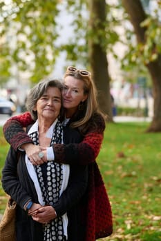 Elderly old cute woman with Alzheimer's very happy and smiling when eldest daughter hugs and takes care of her in park in autumn. Theme aging and parenting, family relationships and social care.