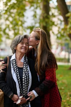 Elderly old cute woman with Alzheimer's very happy and smiling when eldest daughter hugs and takes care of her in park in autumn. Theme aging and parenting, family relationships and social care.