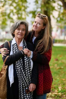 Elderly old cute woman with Alzheimer's very happy and smiling when eldest daughter hugs and takes care of her in park in autumn. Theme aging and parenting, family relationships and social care.