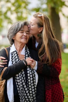 Elderly old cute woman with Alzheimer's very happy and smiling when eldest daughter hugs and takes care of her in park in autumn. Theme aging and parenting, family relationships and social care.