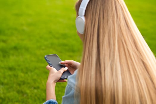 Blonde young woman sits with her back in headphones and listens to music.