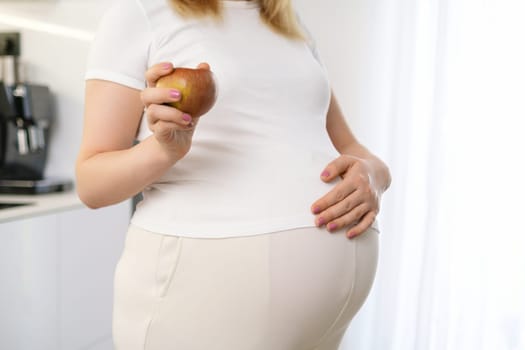 A pregnant woman is holding an apple and put her hand on her stomach. Diet during pregnancy concept.