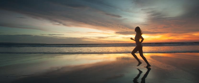 Picture of sexy female running on the beach, in a stylish bikini enjoying summer vacation at sunset copy space background