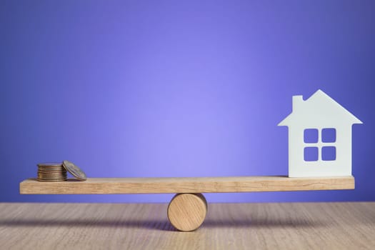 Home insurance. The concept of providing insurance services and real estate security. On the scales lies a stack of coins and a house model on a purple background with copy space. High quality photo