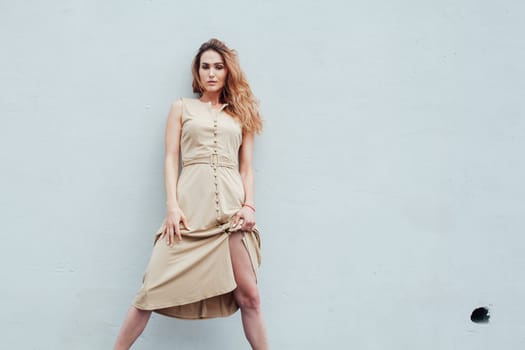 Portrait of a beautiful fashionable woman in a beige dress against a grey background