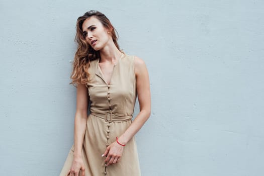 Portrait of a beautiful fashionable woman in a beige dress against a grey background