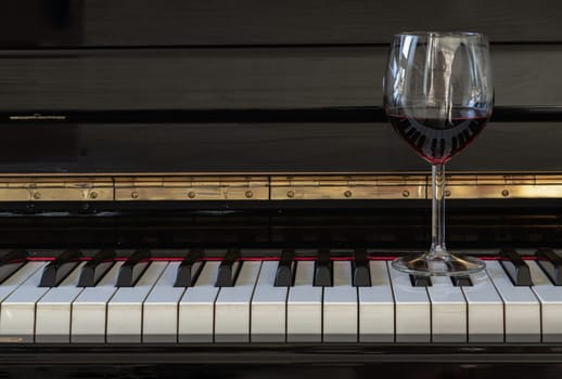 Glass of red wine on piano keyboard. Music and wine concept, Copy space, Selective focus.