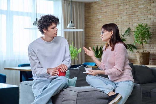 Middle aged mother and son 19, 20 years old talking together at home in living room. Family, relationships, communication mom teenage son, people concept