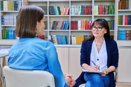 Professional mental therapist college counselor talking to young female student in office with bookcases. Psychologist helping girl overcome difficulties in communication youth mental health concept