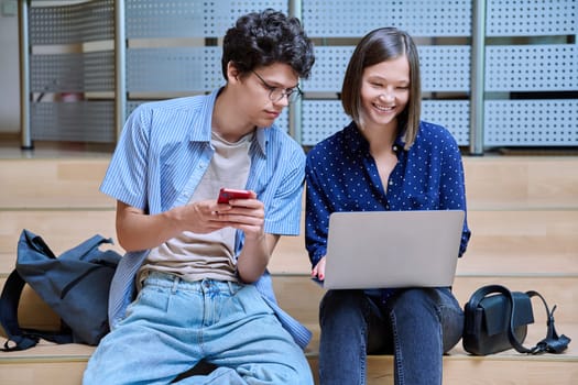 Friends classmates college students guy and girl with smartphone laptop inside educational building. Youth, lifestyle, technology, mobile applications for learning leisure communication