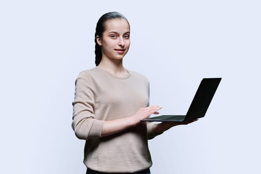 Teen girl high school student using laptop looking at camera on white studio background. Technology, e-learning, education, adolescence, youth concept.
