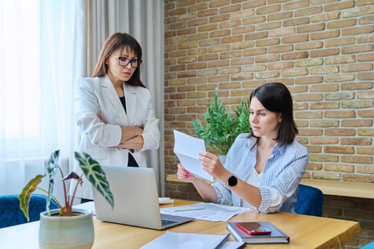 Two serious business women talking working in modern office, young female reading contract document, communicating colleague. Business, ceo, work, law, finance, mentoring, consulting, teamwork, job concept