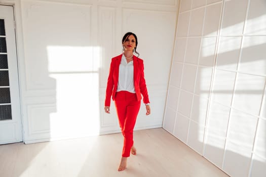 Portrait of a brunette woman in a red business suit in a white room