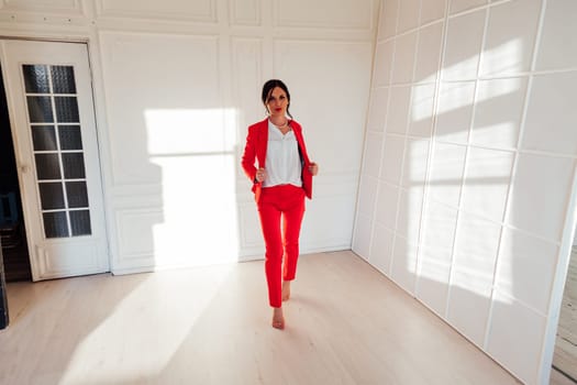 Portrait of a brunette woman in a red business suit in a white room