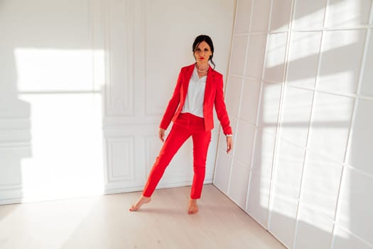 Portrait of a brunette woman in a red business suit in a white room