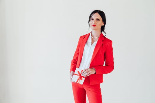 portrait of a brunette woman in a red business suit with a gift in a white room