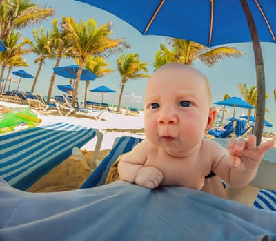 Dad and baby share a tender moment under a beach umbrella, palm trees framing their peaceful bonding.