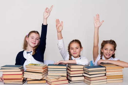 three girls raise their hand up in school class with lots of books