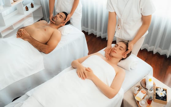 Caucasian couple enjoying relaxing anti-stress head massage and pampering facial beauty skin recreation leisure in dayspa modern light ambient at luxury resort or hotel spa salon. Quiescent