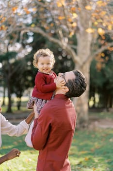 Mom holds a little girl who is raised high in her father arms and hugs his head. High quality photo