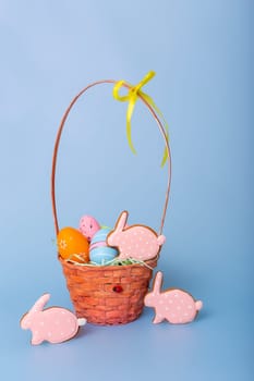 Three pink gingerbread in the form of a rabbit and a basket with decorative Easter eggs stand on a blue background