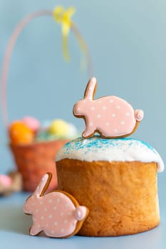 Close up of two pink gingerbread in the form of a rabbit on an Easter cake and a basket with colorful eggs behind