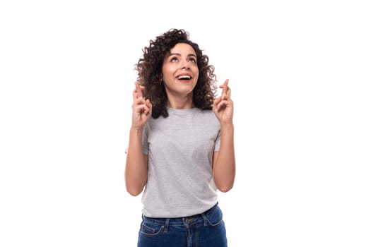 surprised european woman with black curly hair in a gray basic t-shirt points her fingers towards advertising space.