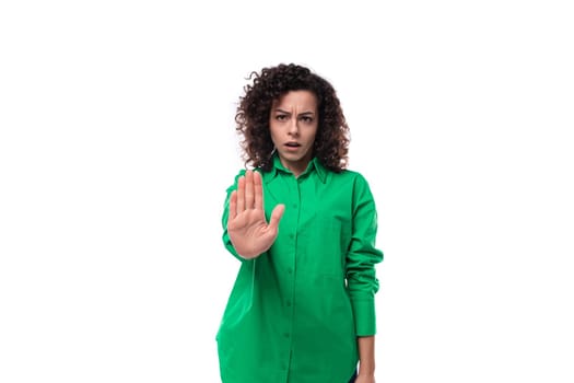 young creative agent woman with curly hair dressed in green shirt showing stop gesture.