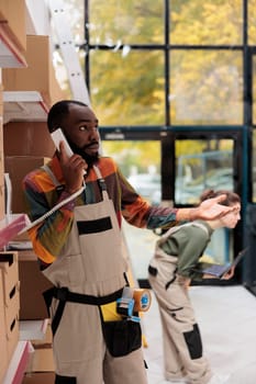 Storehouse manager having remote discussion with supervisor, talking about products quality control at landline phone. African american employee working at customers orders preparing shipment