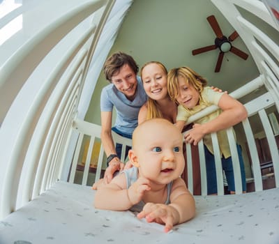 Big family with two kids in white bedroom. Parents and kids standing at crib of newborn baby boy. Boy meeting new sibling. Nursery for infant.