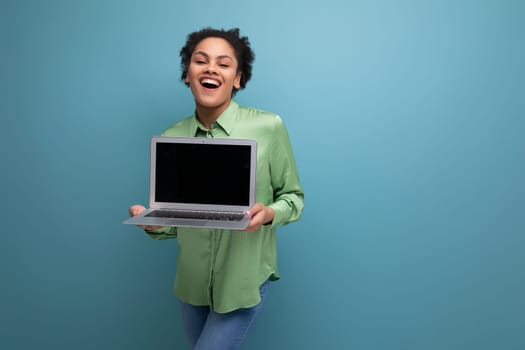 young brunette hispanic woman with curly hair in green rejoices holding a laptop in her hand against the background with copy space.