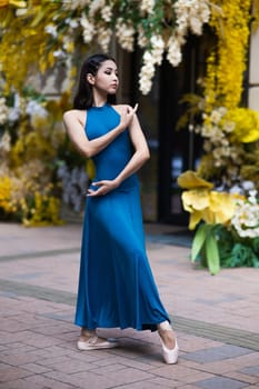 Beautiful Asian ballerina posing against the backdrop of a building decorated with flowers. Vertical photo