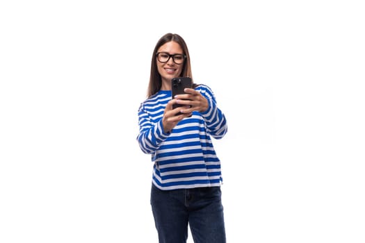 young cute brunette lady in a blue striped casual blouse makes a photo on the phone.