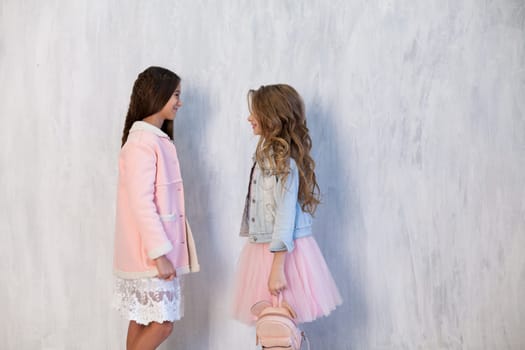 Portrait of two fashionable schoolgirl girls girlfriend in pink clothes on a grey background