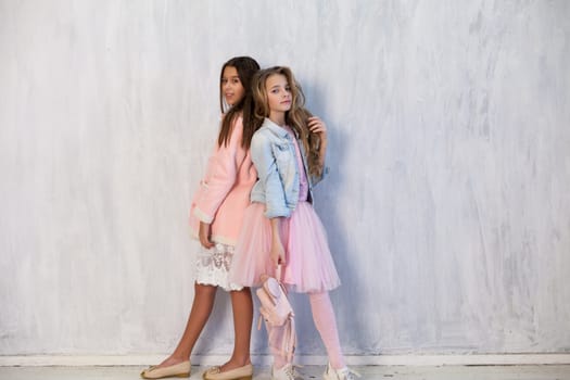 Portrait of two fashionable schoolgirl girls girlfriend in pink clothes on a grey background