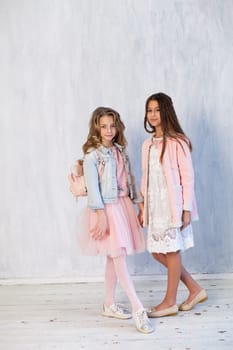 Portrait of two fashionable schoolgirl girls girlfriend in pink clothes on a grey background