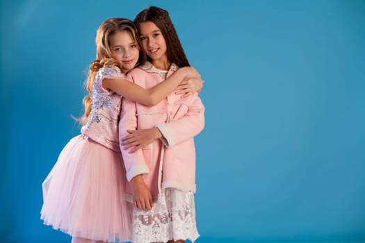 Portrait of two fashionable schoolgirl girls girlfriend in pink clothes on a blue background