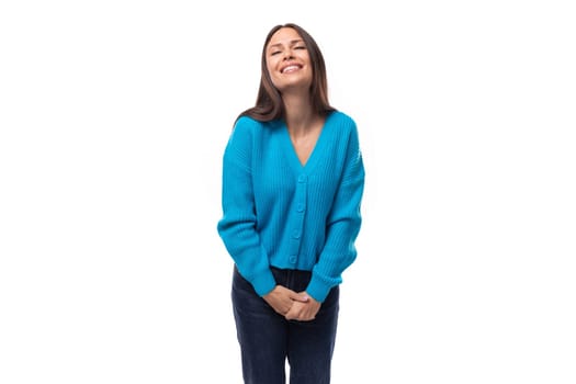 young beautiful slender european brunette woman dressed in a blue cardigan with buttons on a white background with copy space.