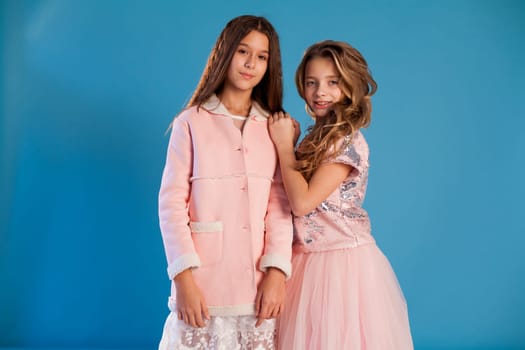 Portrait of two fashionable schoolgirl girls girlfriend in pink clothes on a blue background