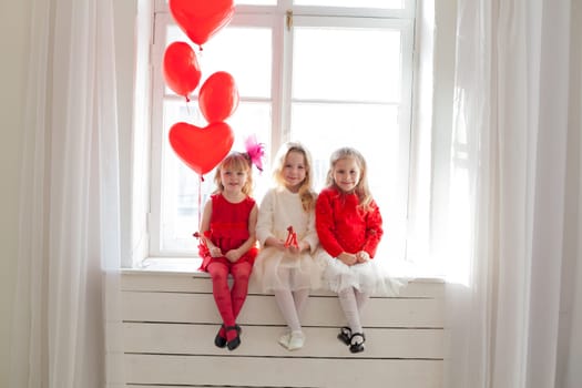 three girls in red and white dresses sitting by the window