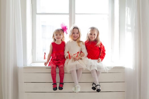 three girls in red and white dresses sitting by the window