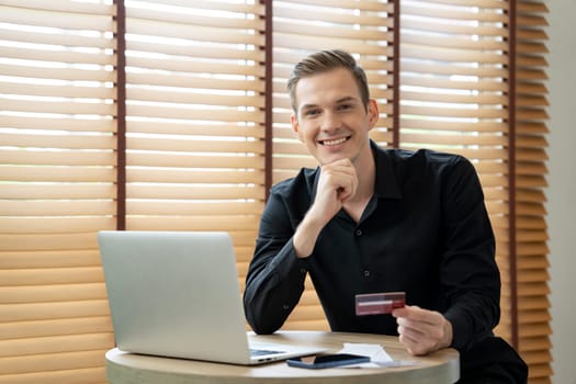 Young man using laptop with credit card for internet banking, online shopping E commerce by online payment gateway at home office. Modern and convenience online purchasing with debit card. Unveiling