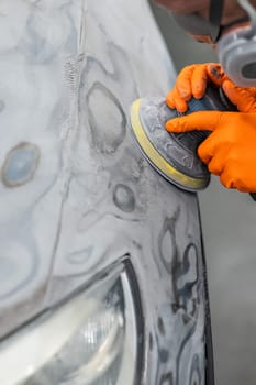 A mechanic sands the putty on a car body with a machine. Repair after an accident. Vertical photo