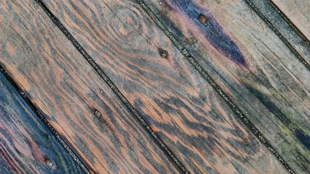 Background of wooden surface made of boards with multicolored spots from humidity, diagonal lines, top view, close-up.