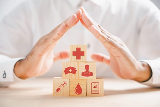 Wooden cube block with health icons and a doctor hand showing protection sign, portraying healthcare and insurance concept. Medical services for a secure future.