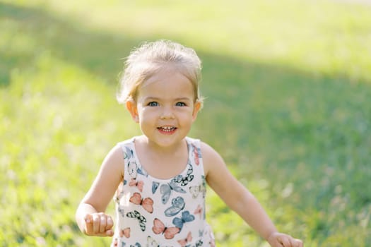 Little laughing girl on a green lawn. Portrait. High quality photo