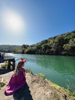 Little girl with Minnie Mouse ears on her head sits on the river bank. High quality photo