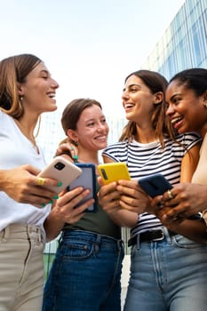 Vertical portrait of happy multiracial group of young women friends laughing and having fun while using mobile phones. Youth lifestyle and social media concept.